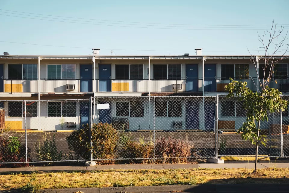 Closed, boarded-up two-story motel behind chain-link fence.